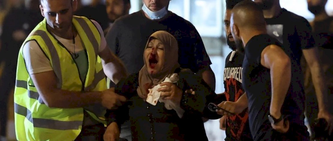 Warga Palestina membantu seorang wanita yang terluka selama protes [Emmanuel Dunand / AFP]