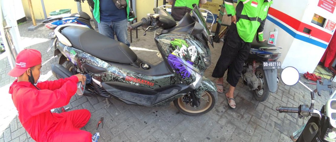 Karyawan Enduro Express sedang melayani ganti oli sepeda motor ojol.