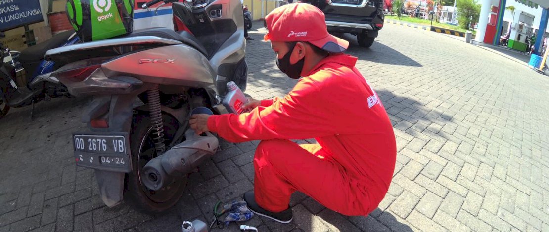 Karyawan Enduro Express sedang melayani ganti oli sepeda motor ojol.