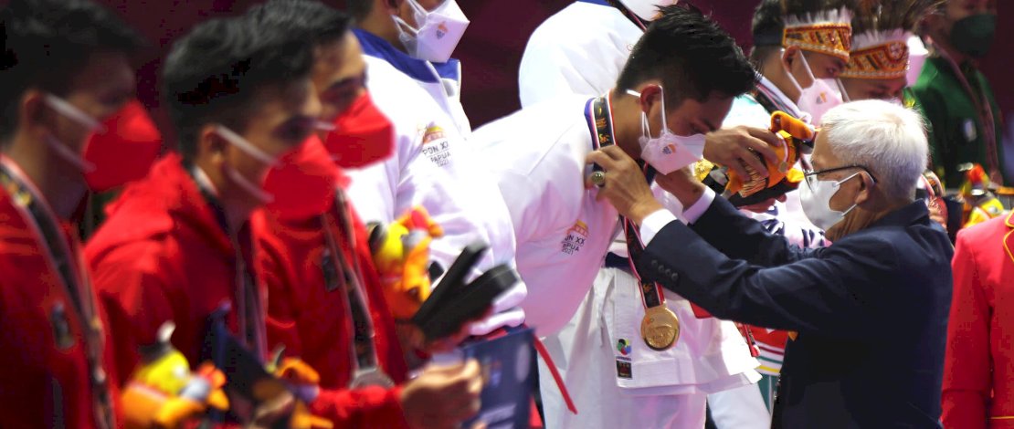 Dewan Hakim PB PON XX Papua Karate, Hendro Gunawan mengalungkan medali emas kepada atlet karate Kata beregu putra Sulawesi Selatan, di GOR Politeknik Penerbangan Kayu Batu Jayapura.