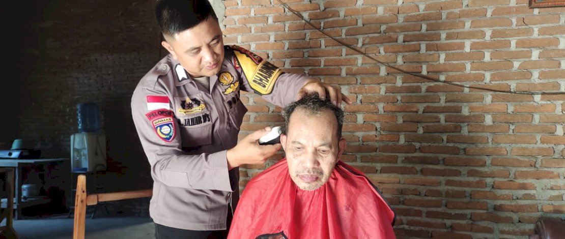 Bripka Aswin Jahar mencukur rambut salah seorang warganya secara gratis.