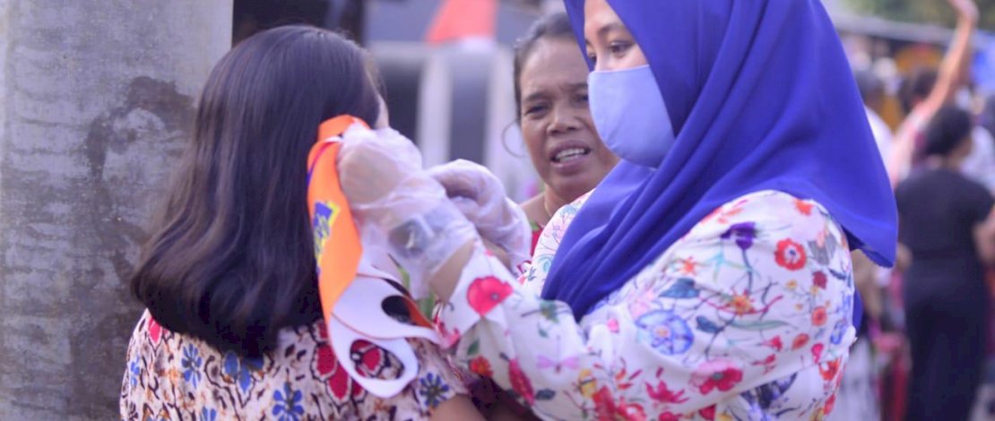 Fatma memasangkan masker ke salah seorang warga.